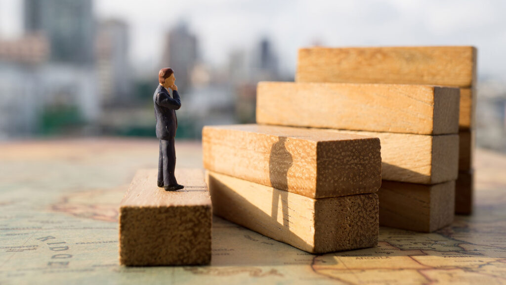 Miniature person standing on wooden step, looking at the next step