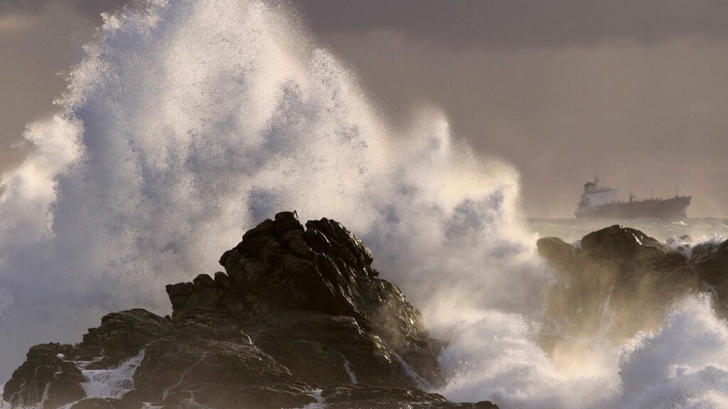 Big waves splashing against rock with boat in the distance